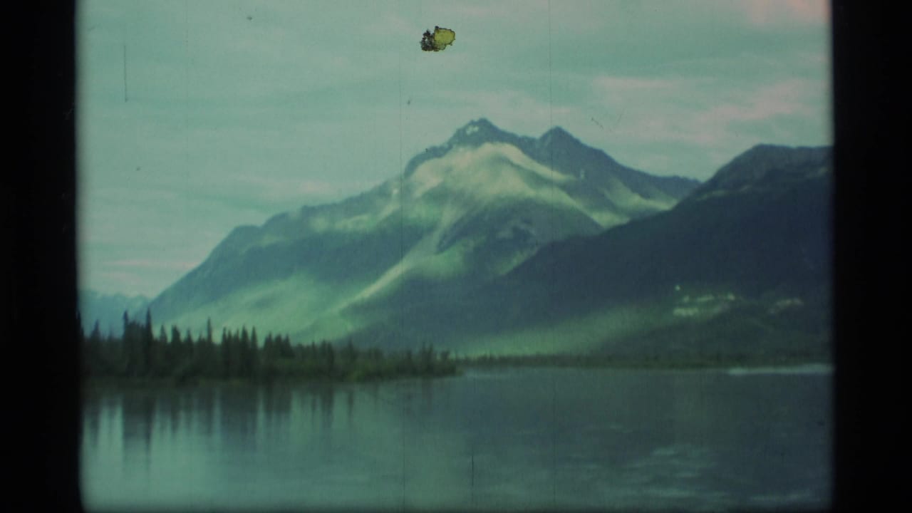 Snow-capped mountains reflected in a calm lake with dark trees along the shore.