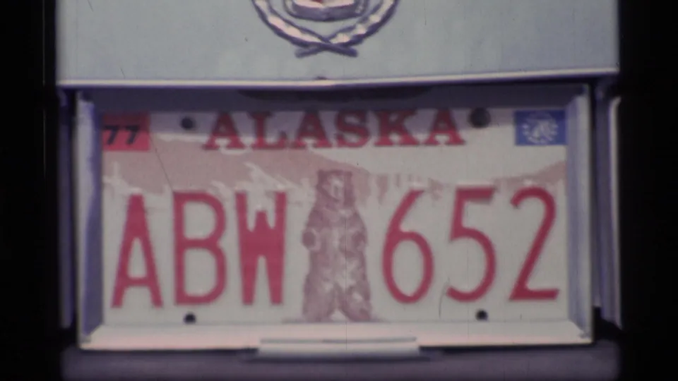 Close 8mm view of a 1977 Alaska license plate reading ABW 652, with a bear emblem and plate frame visible.