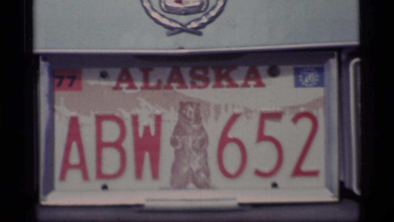 1977 Alaska license plate ABW 6552 with bear emblem, mounted beneath a Cadillac crest in archival 8mm footage.
