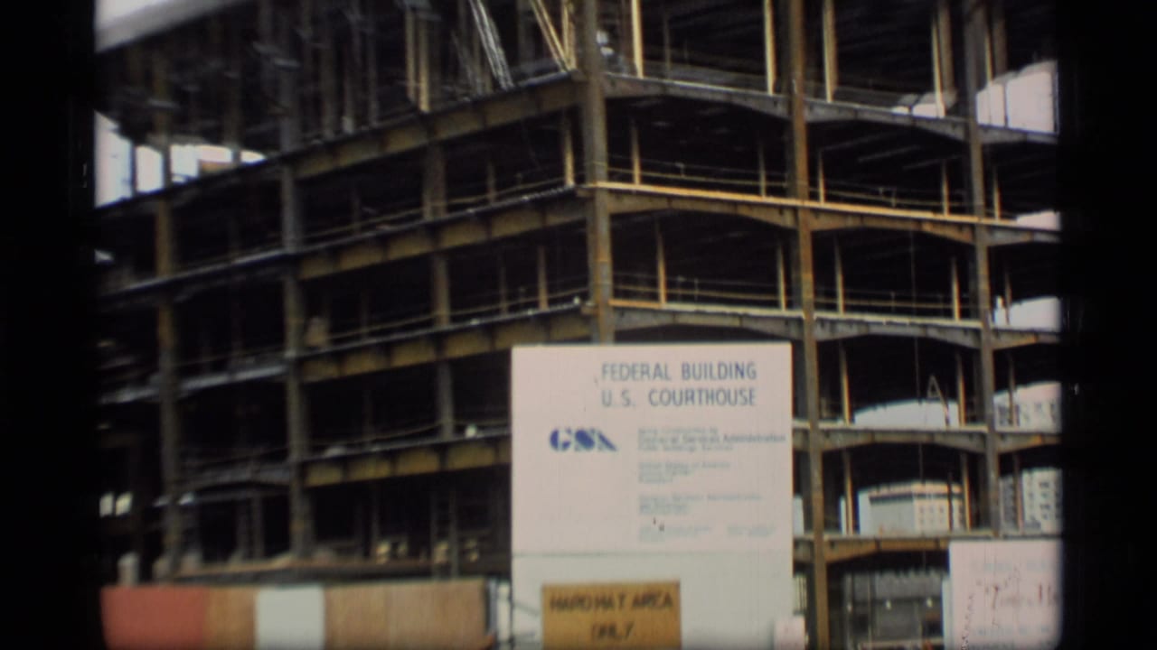 1977 Alaska 8mm frame showing a steel building structure behind temporary fencing and a Federal Building and U.S. Courthouse sign.