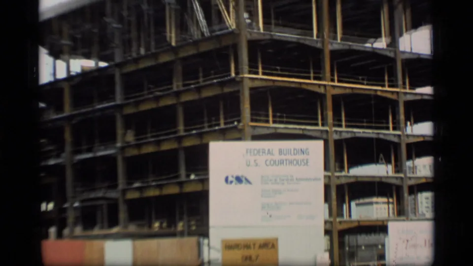 1977 Alaska 8mm frame showing a steel building structure behind temporary fencing and a Federal Building and U.S. Courthouse sign.