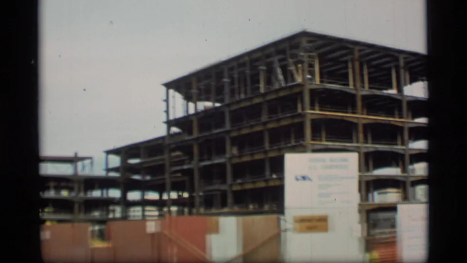 Handheld 8mm view of the Alaska federal building construction site, with steel framing, fencing, and a sign in front.