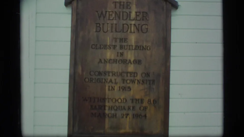 Final 1977 Alaska frame holding on the Wendler Building sign, its weathered wood and dark lettering visible against pale clapboard.