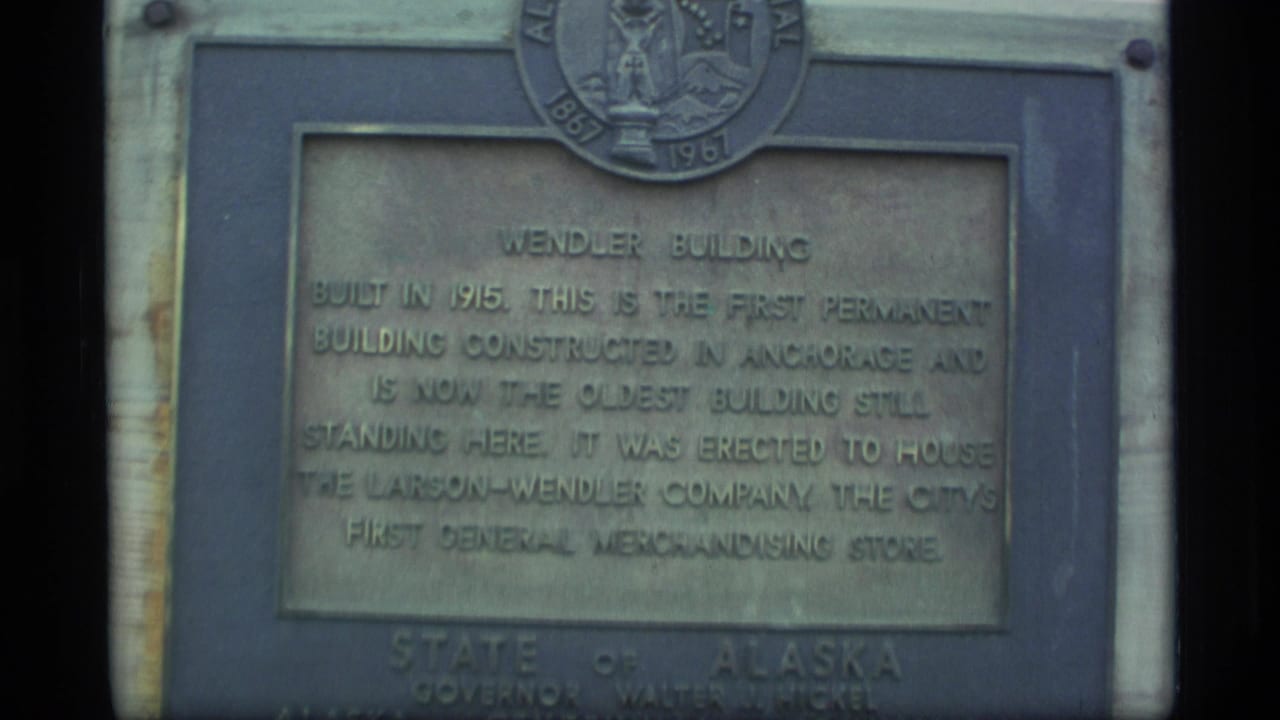 Close 1977 Alaska 8mm view of a weathered Wendler Building plaque with the Alaska state seal above the inscription.