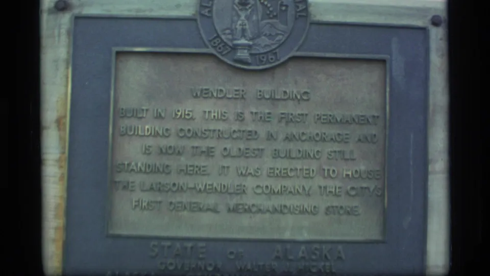 Close 1977 Alaska 8mm view of a weathered Wendler Building plaque with the Alaska state seal above the inscription.