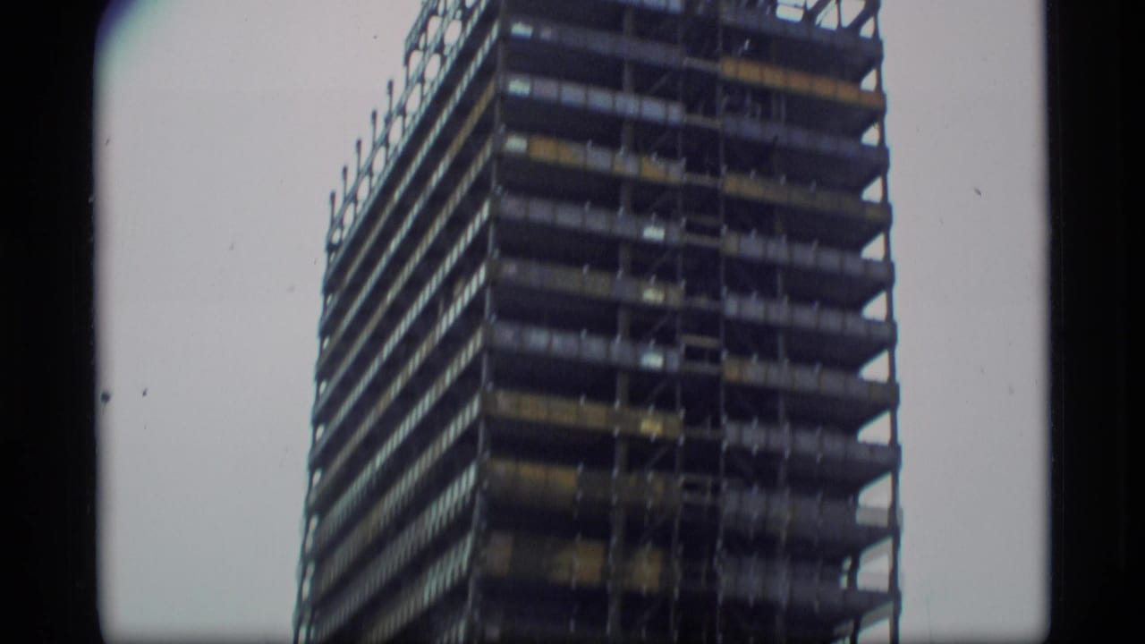1977 Alaska home-movie frame showing a tall unfinished high-rise building under construction, partially cropped by handheld 8mm framing.