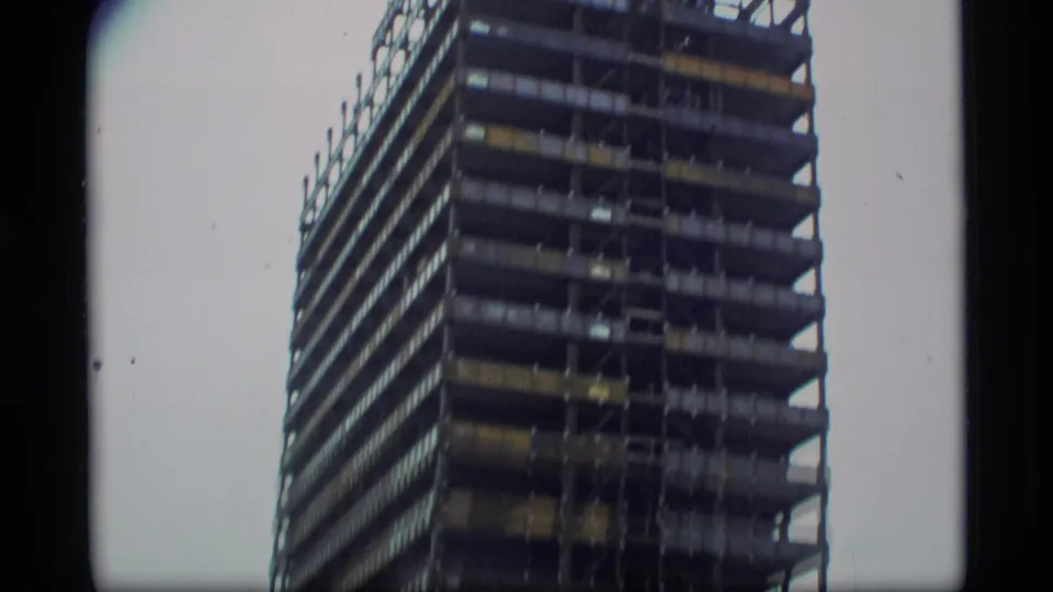 1977 Alaska home-movie frame showing a tall unfinished high-rise building under construction, partially cropped by handheld 8mm framing.