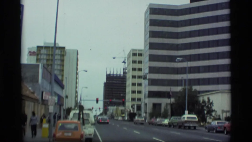 1977 Alaska street view with cars, distant pedestrians, streetlights, and modern commercial buildings.