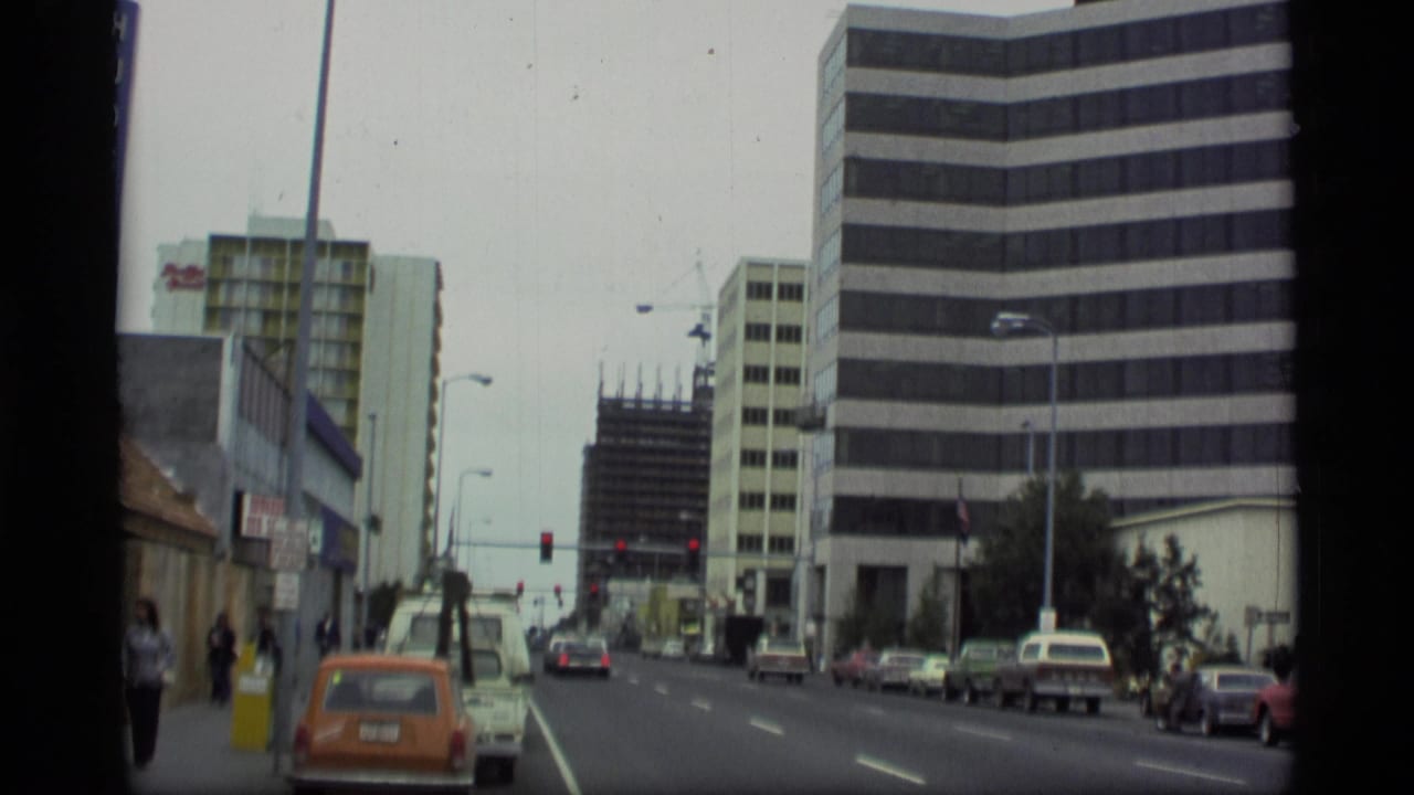 Similar city street view with traffic, pedestrians, office buildings, and a crane in the distance.