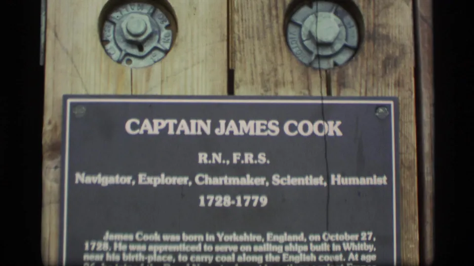 1977 Alaska 8mm frame showing a close view of a Captain James Cook plaque with biographical text mounted on vertical wood boards.