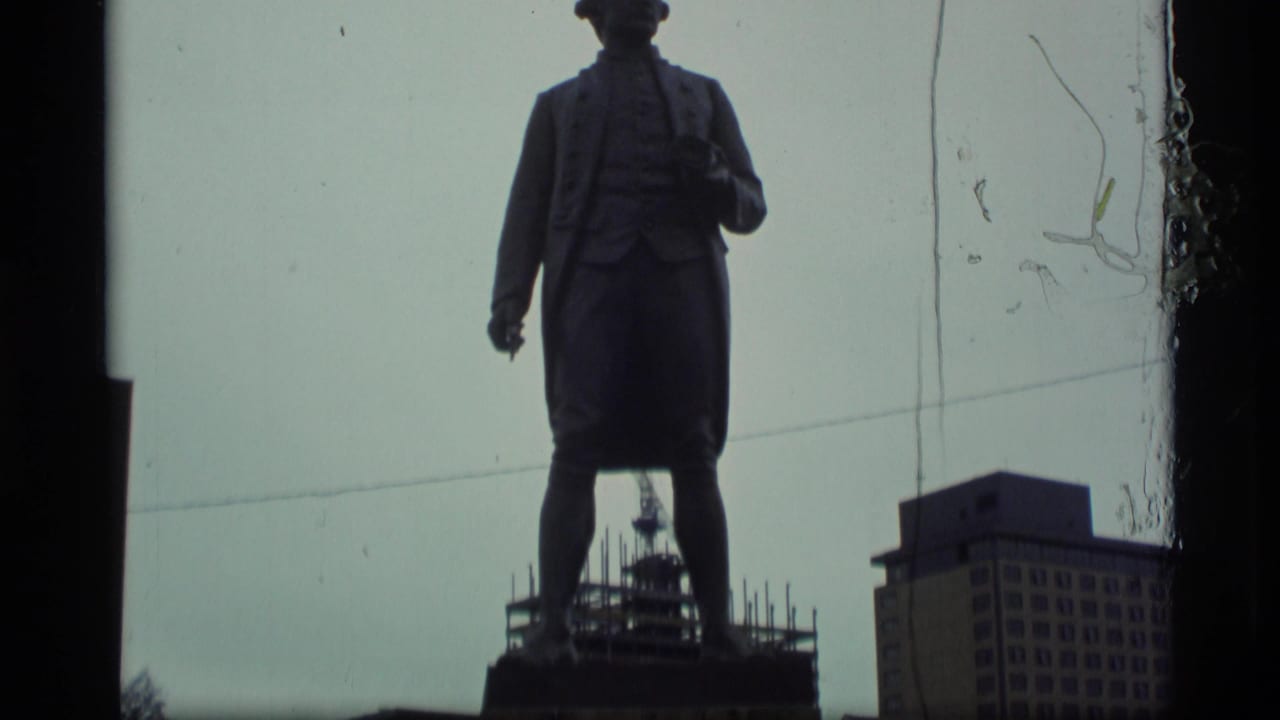 Silhouetted statue of Captain James Cook with buildings in the background.