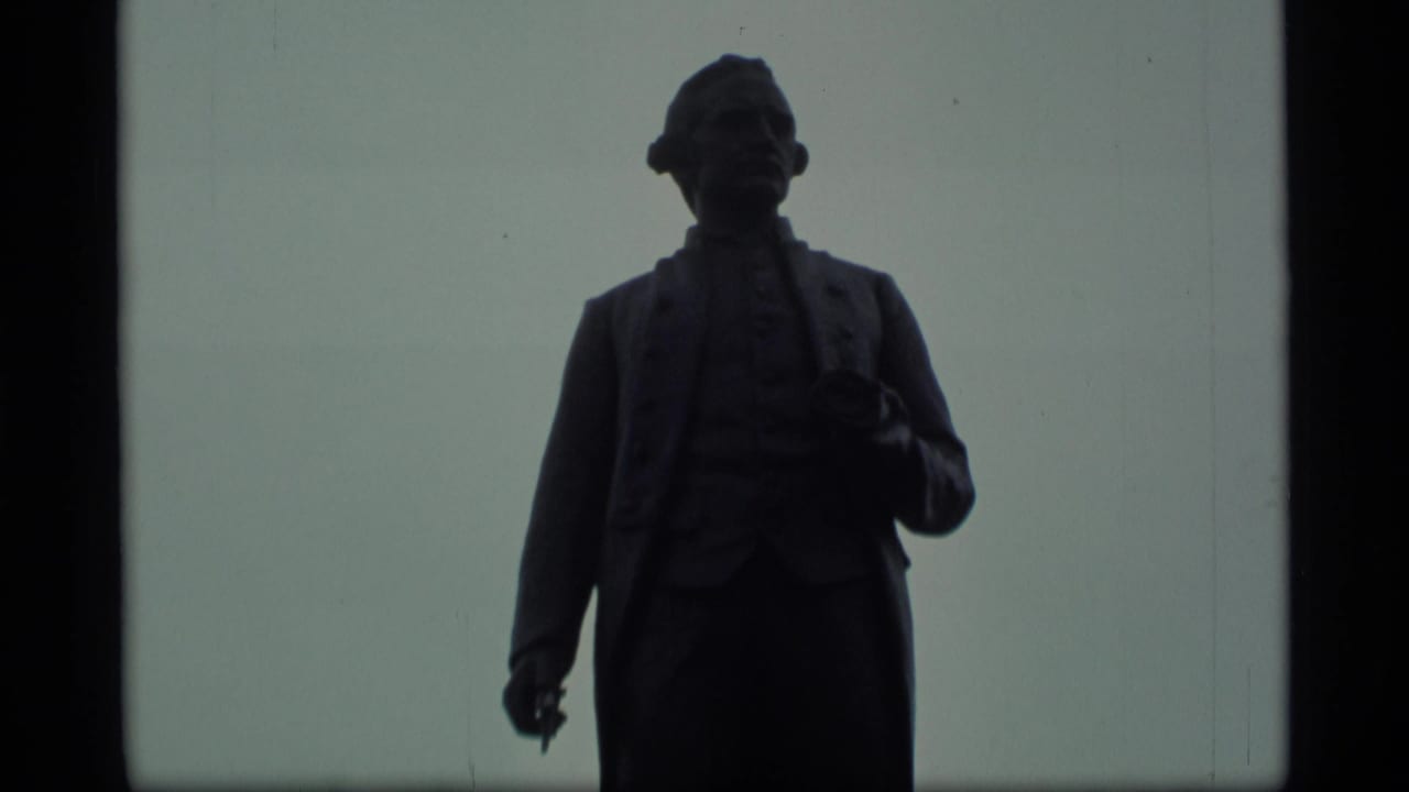Dark silhouetted statue against a pale overcast sky.