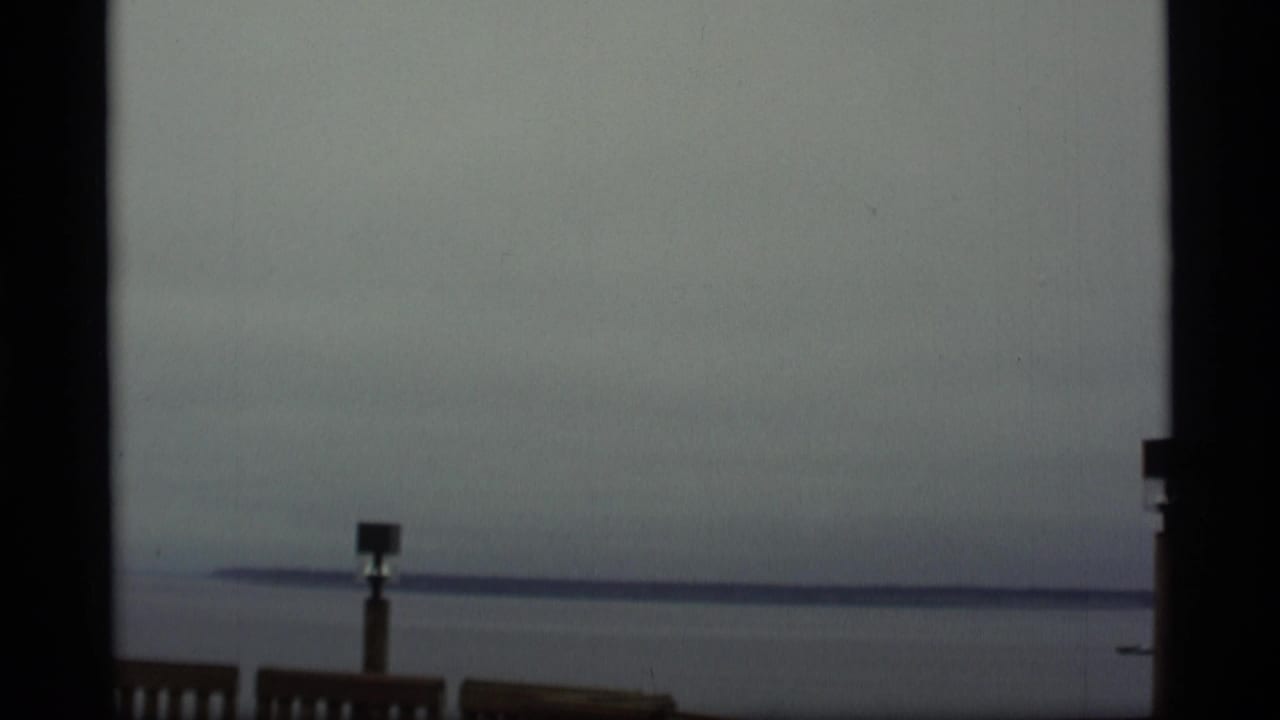 1977 Alaska 8mm coastal view with gray water, a low horizon, and a wooden post near the bottom of the frame.