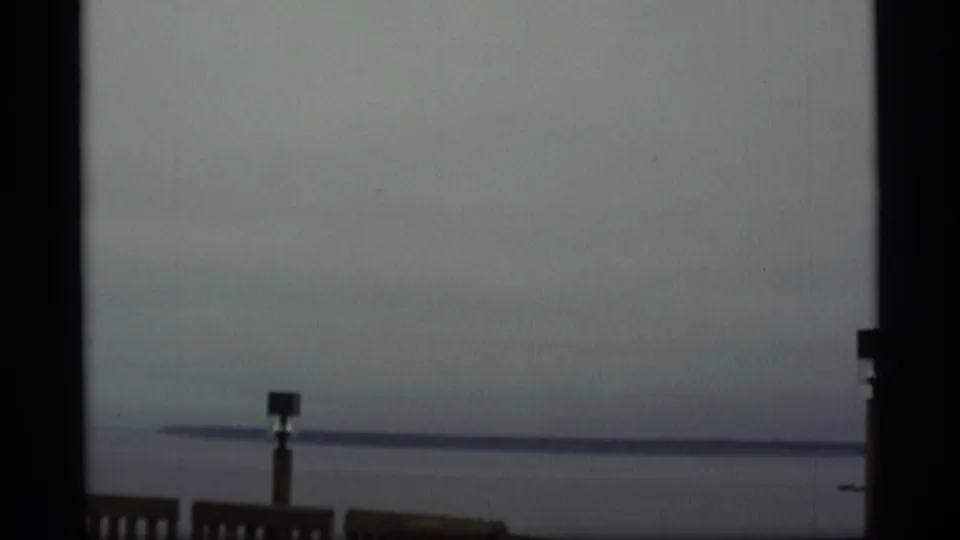 1977 Alaska 8mm coastal view with gray water, a low horizon, and a wooden post near the bottom of the frame.