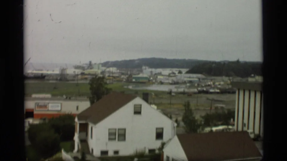 Soft 8mm frame from Alaska in 1977 with houses in the foreground and a working harbor landscape beyond the fields.