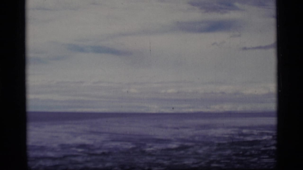 Soft 8mm frame of a lake horizon beneath a cloudy sky, bordered by dark film edges.