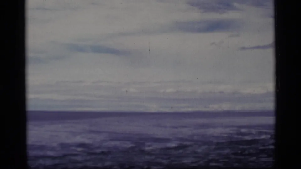 1977 Alaska 8mm frame showing a muted lake horizon under layered clouds, with soft focus and visible film gate edges.