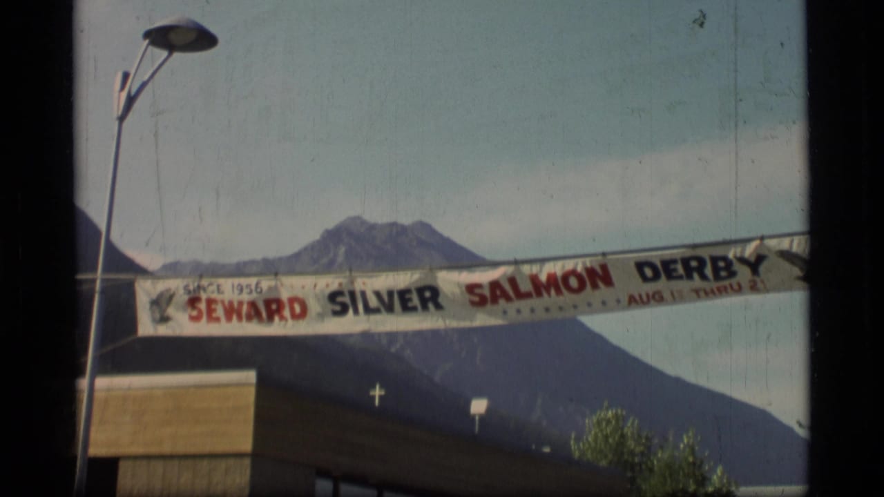1977 Alaska 8mm frame showing a Seward Silver Salmon Derby banner, street lamp, building edge, and mountain backdrop.