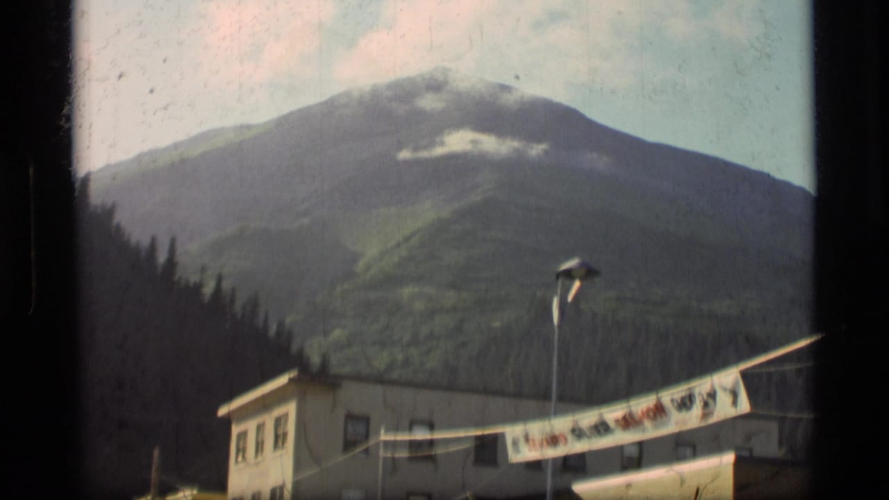Mountain slope behind a low building and streetlight, with a banner across the foreground.