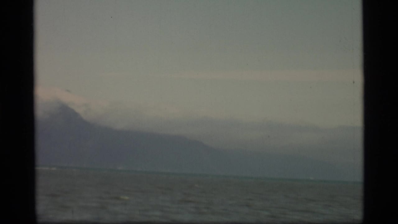 Hazy ocean with distant mountain silhouettes framed by dark film borders.