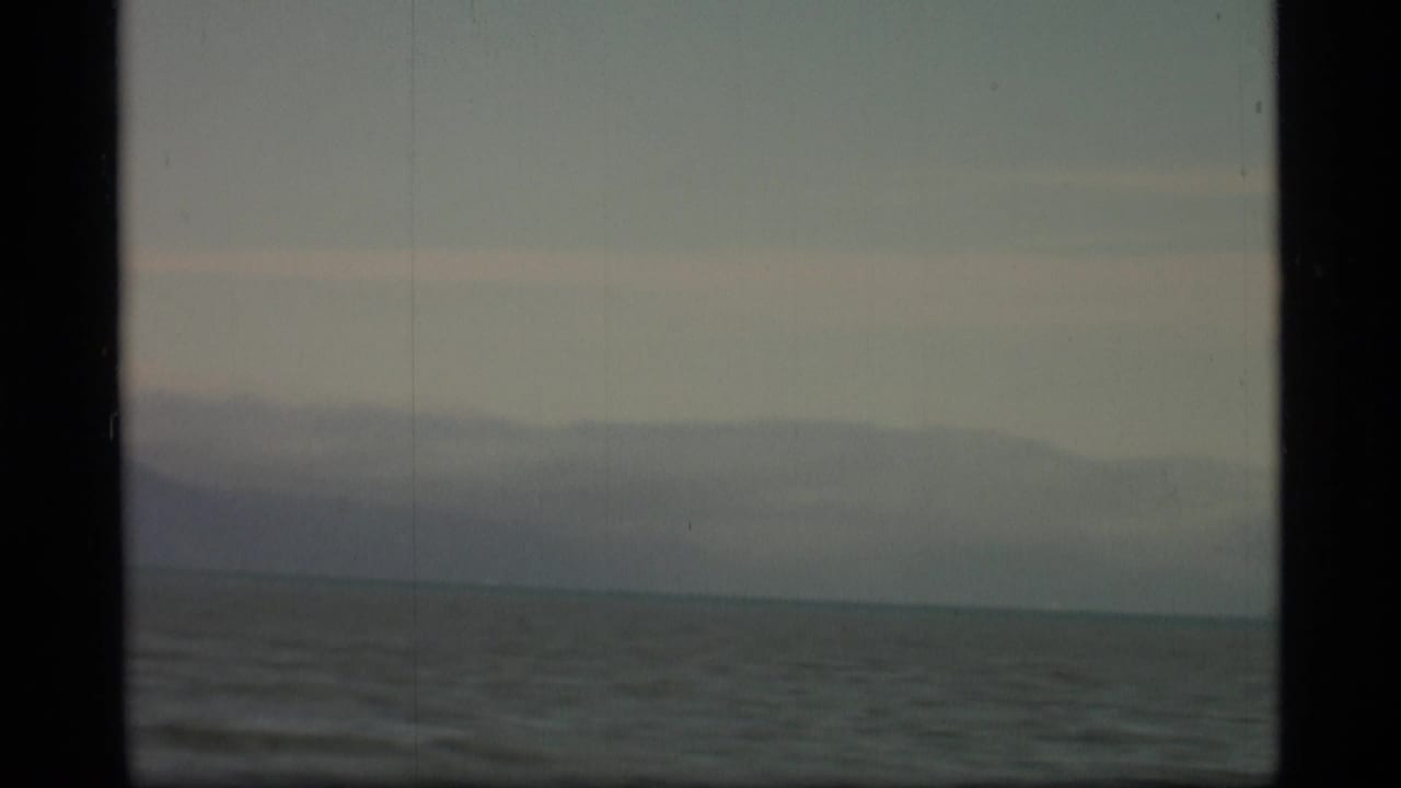 Open water and distant mountains seen through a dark projector frame.