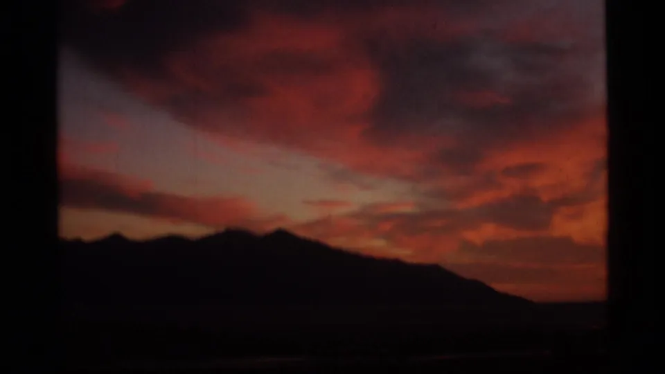 1977 Alaska 8mm frame with a dark mountain ridge against saturated red and orange sunset clouds.