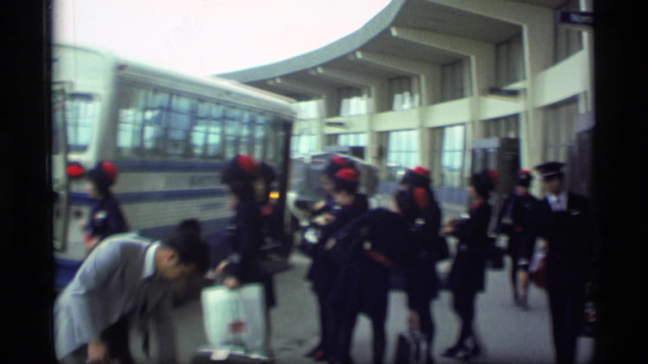 Passengers and flight attendants in dark uniforms with red hats stand beside a Servair bus outside the Alaska terminal.