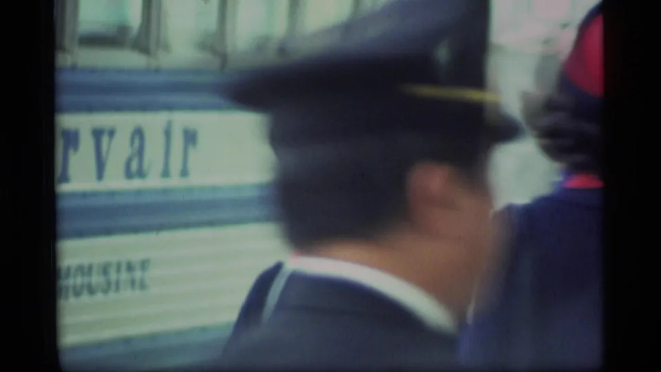 Soft close view of a uniformed man passing in front of Servair bus lettering during the 1977 Alaska airport scene.