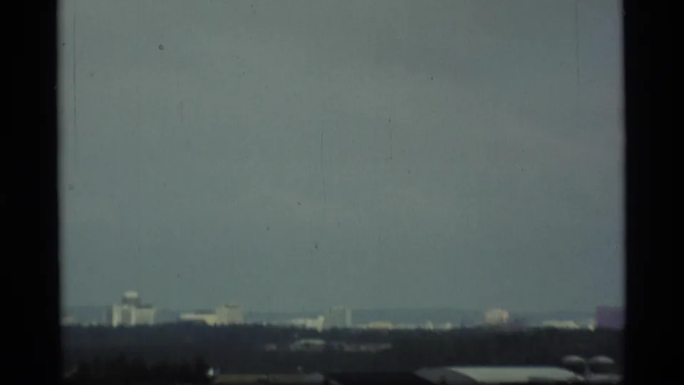The frame holds on an overcast cityscape with distant blocky buildings and a dark foreground band, matching the clip's Alaska metadata.