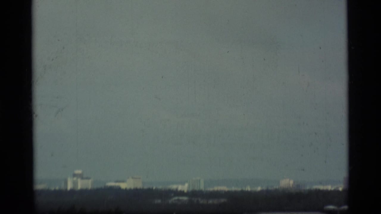 Distant hazy city skyline seen beyond a dark foreground and overcast sky.