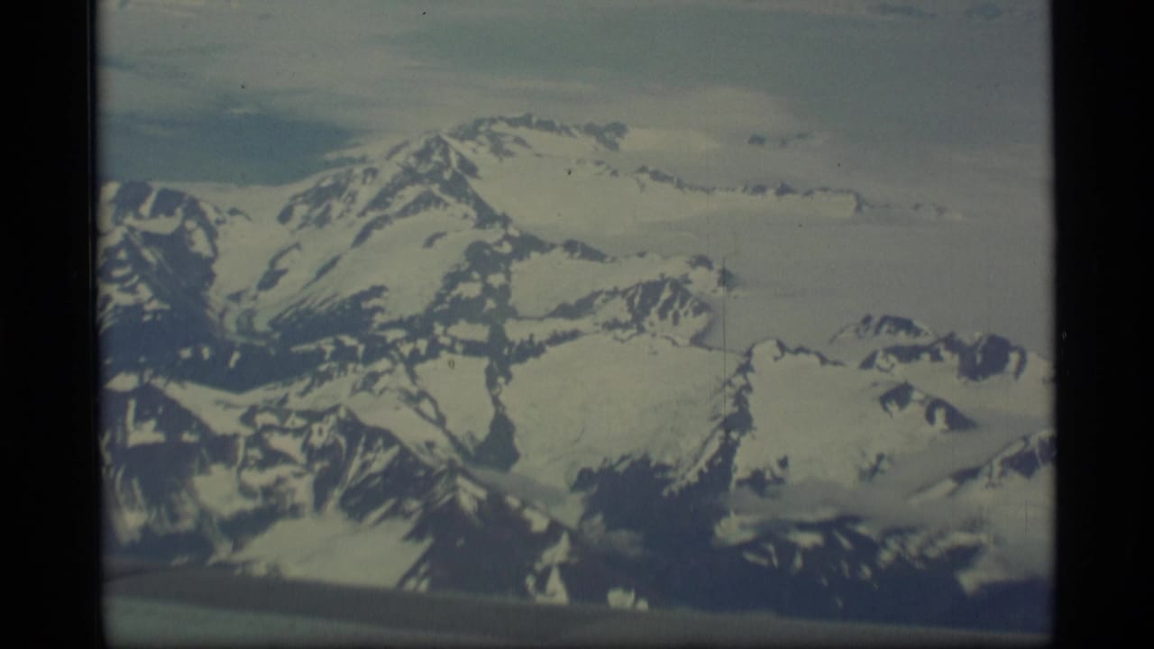 Aerial view of broad snowy peaks and glacier-covered terrain through a film frame.