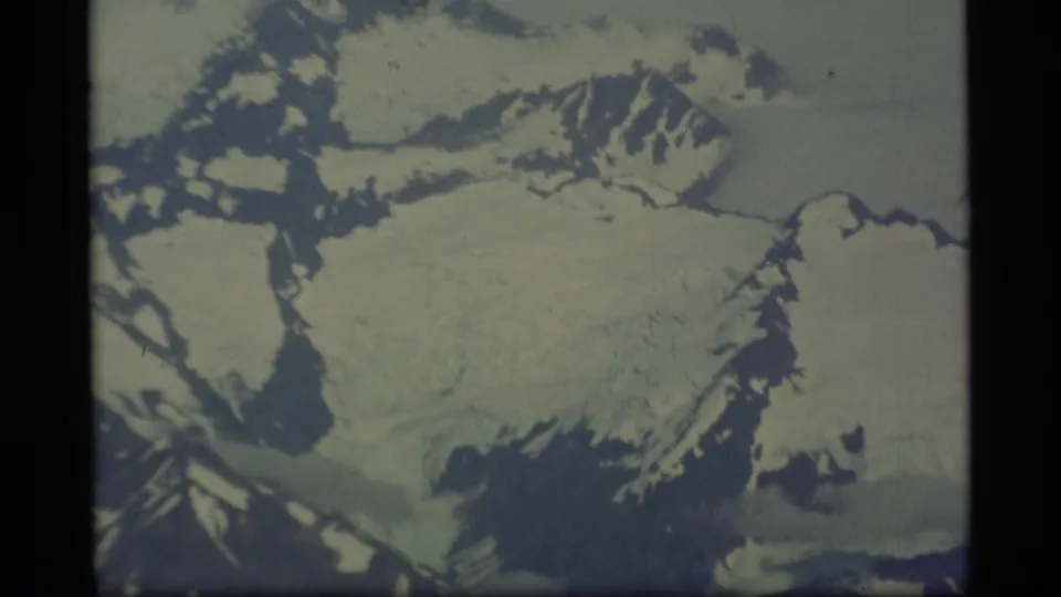1977 Alaska 8mm frame showing a broad glacier-like snowfield with dark rock margins and nearby mountain slopes.