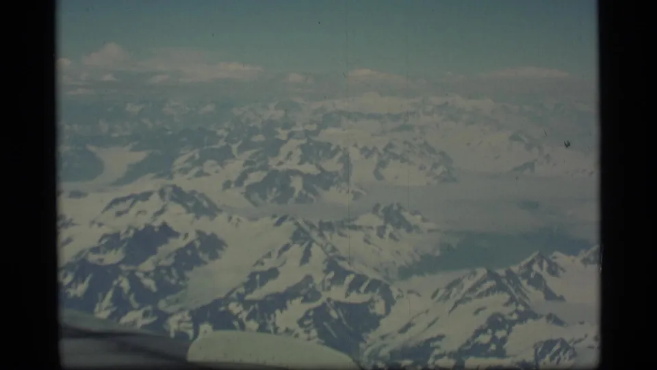 1977 Alaska aerial home-movie view of snowy mountain ridges and broad icy terrain filmed through an airplane window.