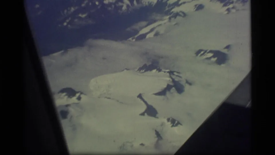 A faded 8mm aerial view over Alaska snowfields, glacier ice, and mountain ridges from a passenger window.