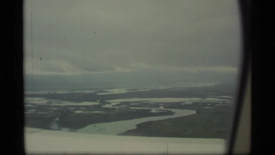 1977 Alaska 8mm frame showing winding water channels, wetland patches, open low land, overcast sky, and visible film-frame borders.