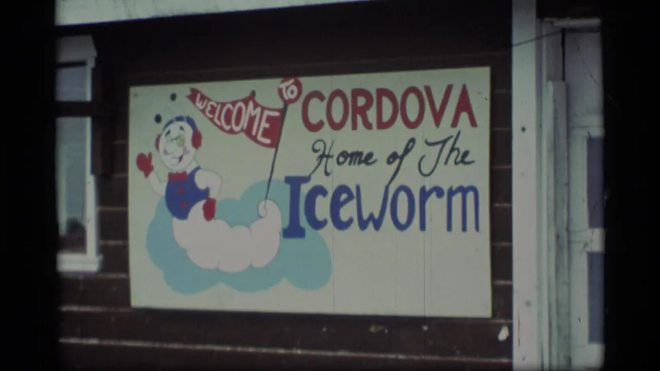1977 Alaska 8mm view of the Cordova 'Home of The Iceworm' sign with a painted mascot on a building facade.