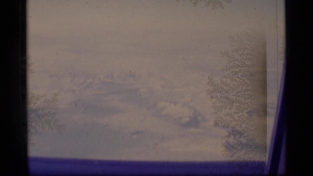 1977 Alaska 8mm frame showing distant snowy peaks through frost-patterned window glass and dark frame borders.