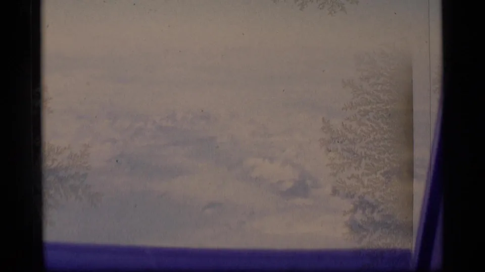 1977 Alaska 8mm frame showing distant snowy peaks through frost-patterned window glass and dark frame borders.
