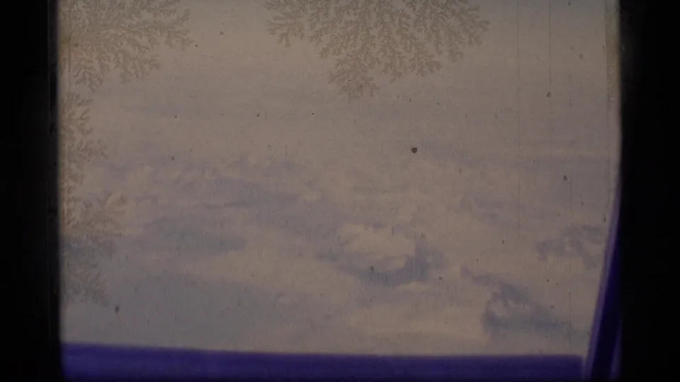 A static 1977 Alaska home-movie view of snowy peaks beyond frost crystals on a window pane.