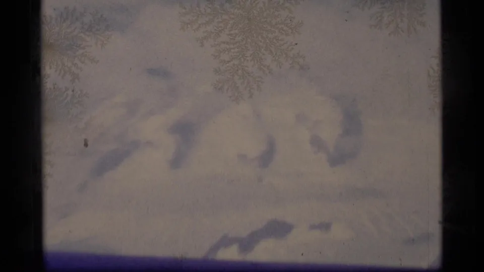 Snow-covered Alaska peaks appear faintly through frosty glass in a softly exposed 8mm frame from 1977.