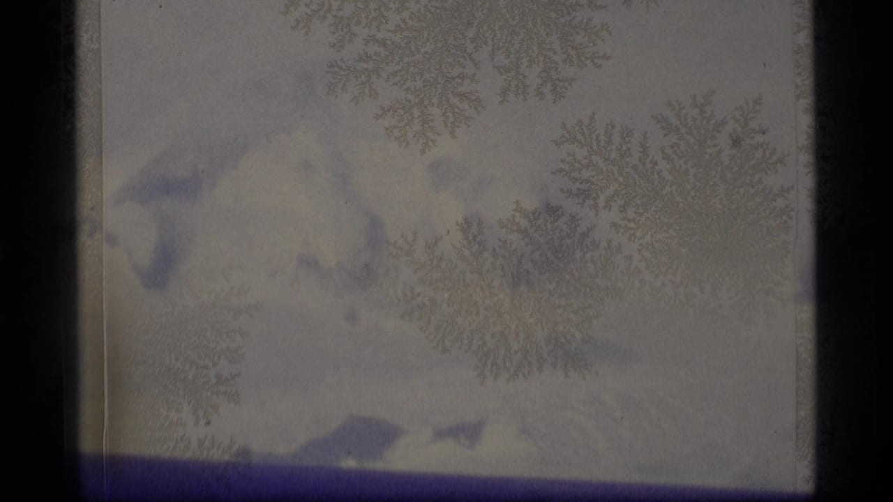 1977 Alaska 8mm frame with pale sky, distant snowy mountains, and frost-like crystals obscuring much of the view.
