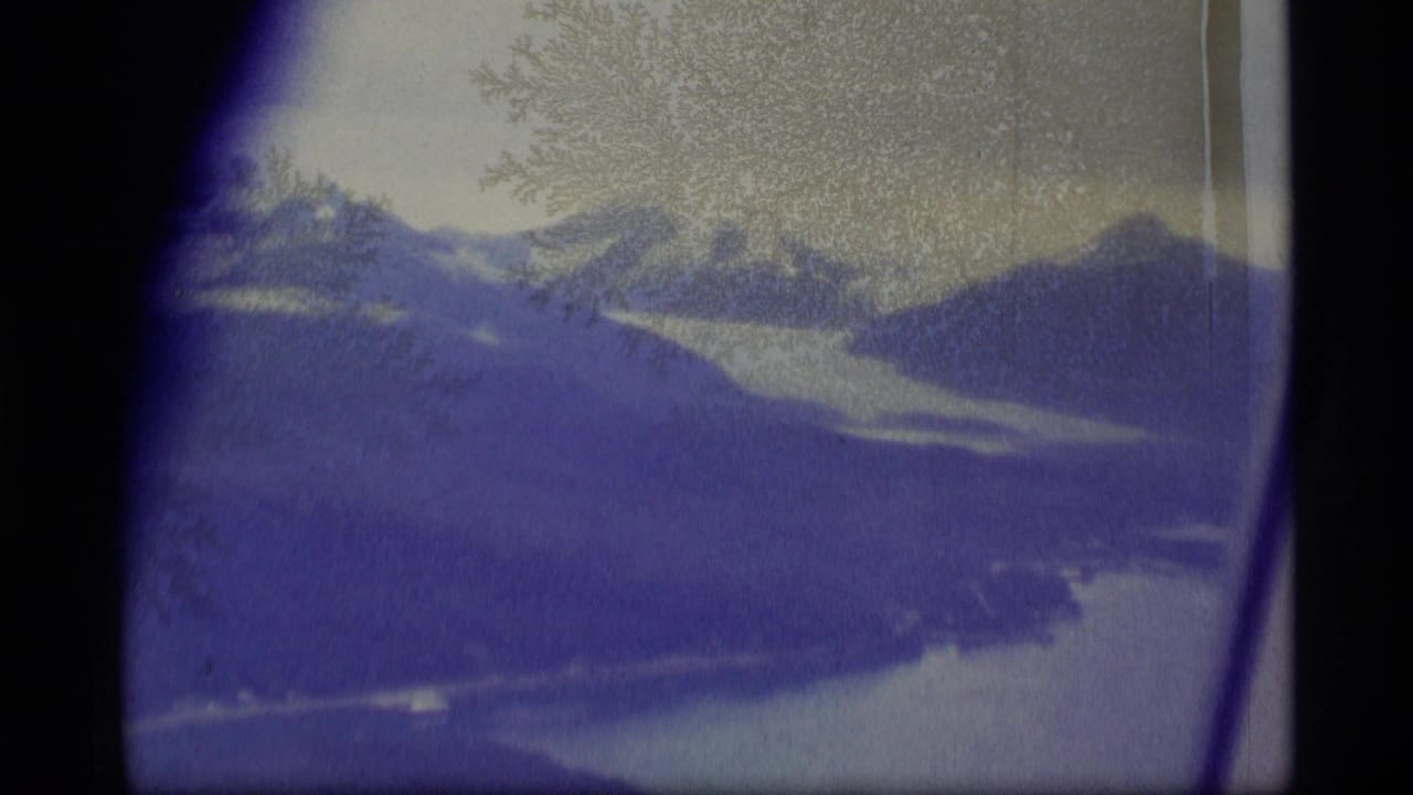 1977 8mm Alaska aerial view showing mountain ridges, pale water, window edges, and visible film texture.