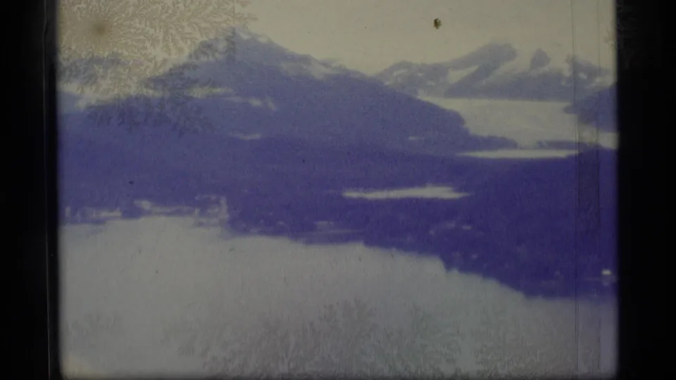 1977 Alaska 8mm frame showing snowy mountains beside a lake, with strong frost-like crystalline patterns over the scene.