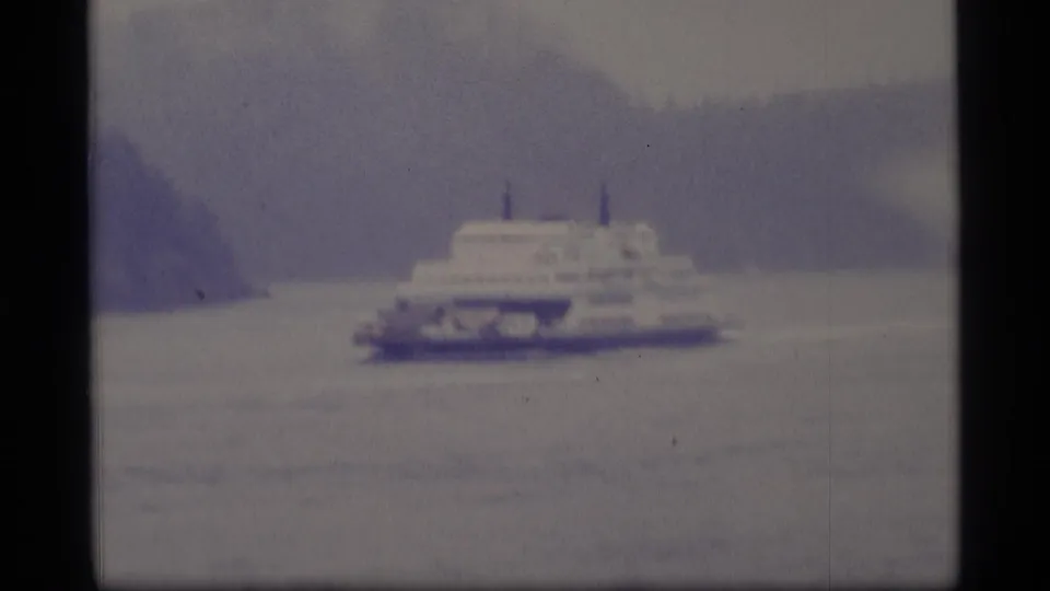 1977 Alaska 8mm frame showing the ferry broadside near a wooded shoreline, with soft focus and muted home-movie color.