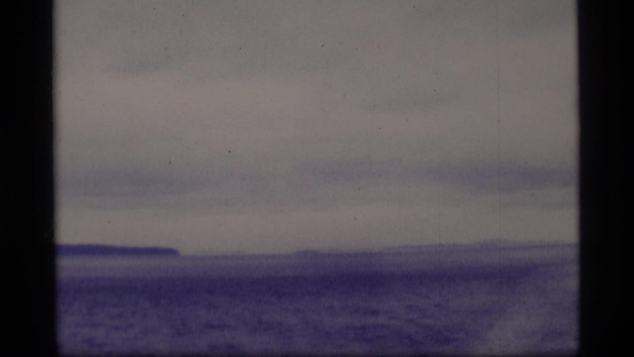 Muted overcast water or ice with a distant low shoreline, seen through dark vertical frame edges.