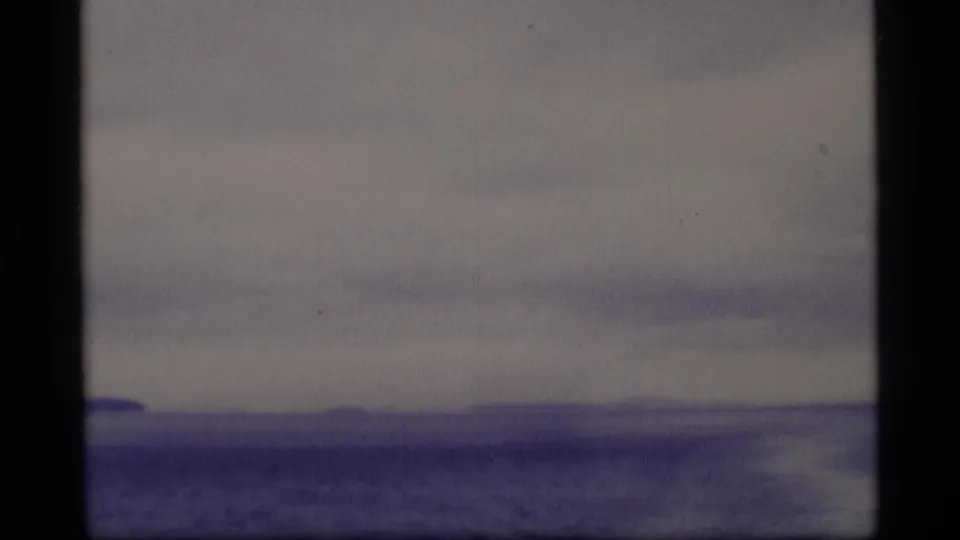 Soft 8mm Alaska travel view with a low distant shore, cloudy sky, and dark vertical framing in the foreground.