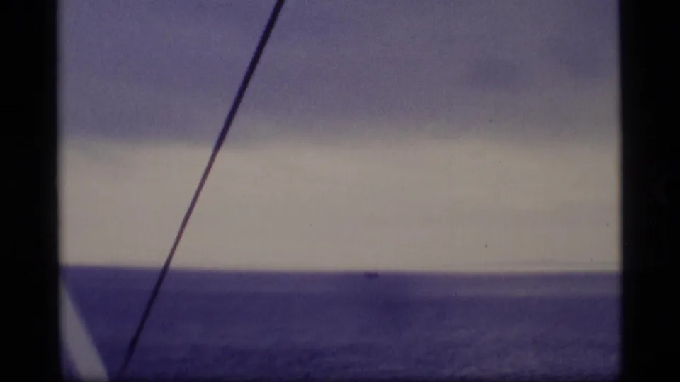 1977 Alaska 8mm maritime view showing a calm sea horizon, cloudy sky, diagonal boat cable, and possible distant vessel.