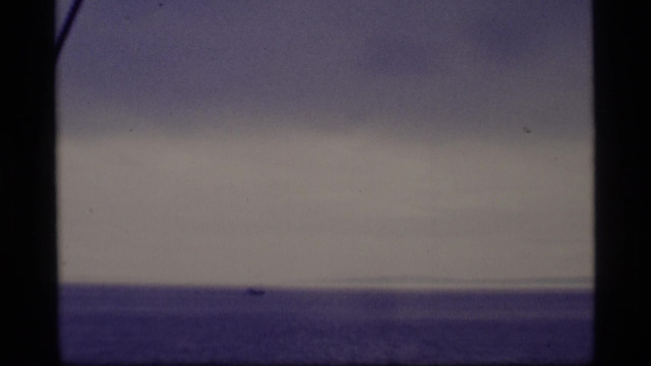 Distant small boat on calm ocean beneath a muted sky.