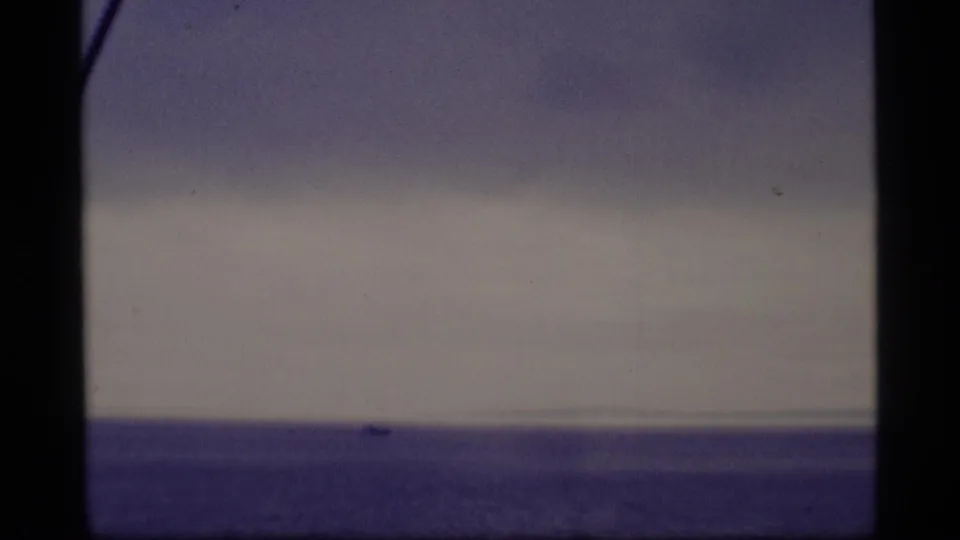 1977 Alaska 8mm frame with a small distant boat near the horizon on calm open water under an overcast sky.