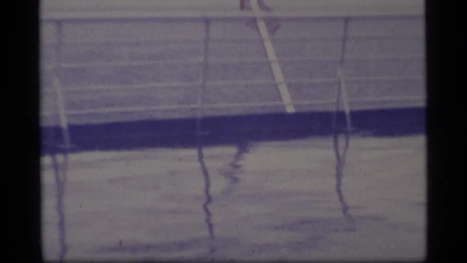 1977 Alaska home-movie frame showing wet deck railings and a small American flag near the right edge.
